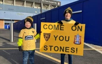 Two young Maidstone United fans hold a sign saying 'Come on You Stones'