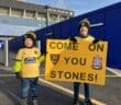 Two young Maidstone United fans hold a sign saying 'Come on You Stones'