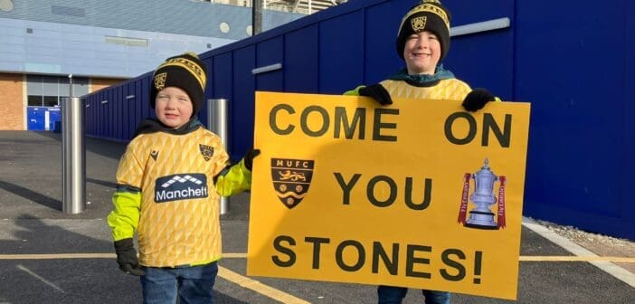 Two young Maidstone United fans hold a sign saying 'Come on You Stones'